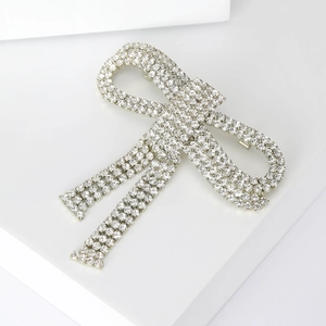 Close-up of a sparkling silver bow brooch with pavé rhinestones on white display stand