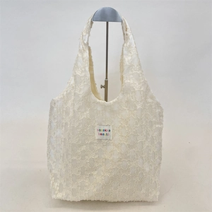 Detail of floral jacquard texture and branded patch on cream lace tote bag