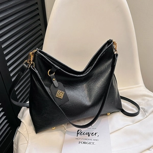 Large black pebbled leather tote bag with gold hardware on a minimalist chair