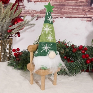 Detail of a Christmas gnome figurine with green knitted hat on a mini wooden chair