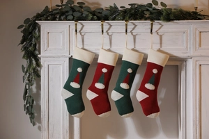 Detail of red and green knitted Christmas stockings with 3D santa hat design on mantel