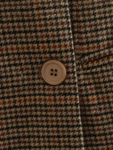 Détail macro du tissu pied-de-poule marron et du bouton marron clair mat du blazer