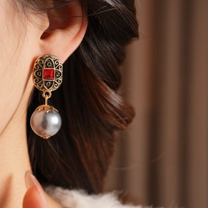 Detail von Vintage-Goldohrringen mit roten Steinen und grauen Perlen an einem Model