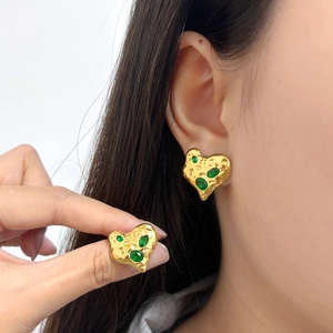 Golden heart earrings with green gemstones and hammered texture worn on a female model