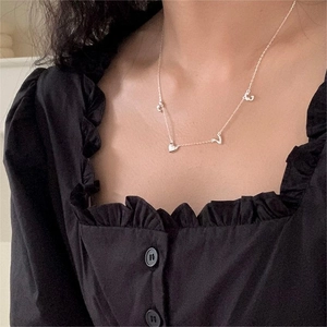 Close-up of minimalist silver LOVE necklace with heart and floral charms on a model