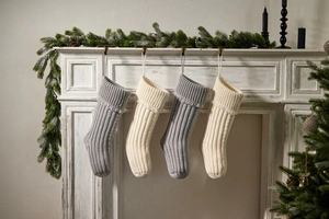 Close-up of knitted Christmas stockings in cream and grey hanging on a festive fireplace