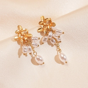 Détail de boucles d'oreilles fleur dorée avec pompons perles sur soie champagne élégante