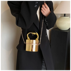 Detail of a gold cylindrical metal handbag with a unique irregular ring handle and chain