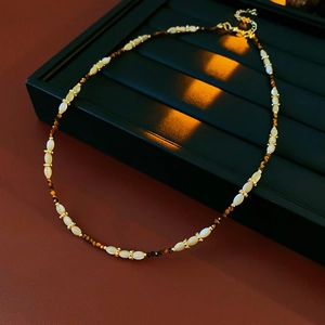 Détail du collier de perles blanches et dorées posé sur une boîte à bijoux sombre chic