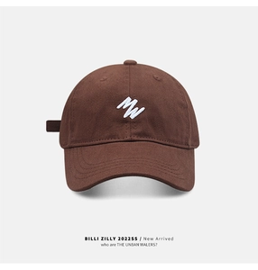 Detailed close-up of white MW embroidery on a dark brown cotton twill baseball cap