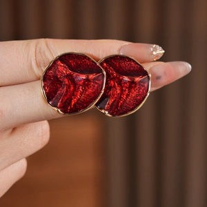Close-up of red enamel round stud earrings with textured gold trim held by hand