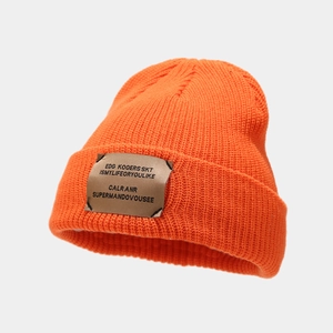 Detail of orange knitted beanie with ribbed texture and brown woven patch on fold
