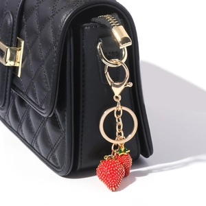 Macro shot of realistic red strawberry charms on a quilted black leather handbag