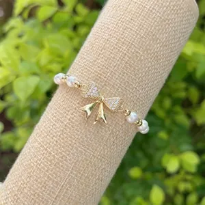 Macro detail of 18K gold-plated bow charm with sparkling crystals on a pearl bracelet