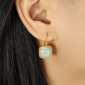 Elegant gold square earrings with light green jade stone, shown on a female model