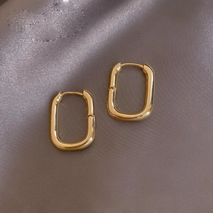 Detailed top view of gold geometric rectangular hoop earrings on smooth silk fabric