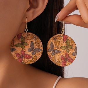 Detail shot of large cork drop earrings with colorful butterfly print on a female model