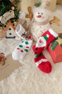Détail de chaussettes de Noël en polaire corail avec motifs Père Noël et renne sur un tapis