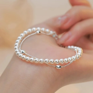 Elegante bracciale a doppio strato con perle bianche e sfere d'argento al polso di una donna