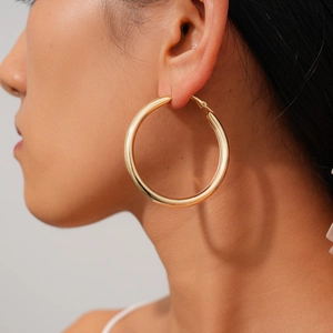 Close-up of a large polished gold hoop earring worn by a model in a minimalist profile view