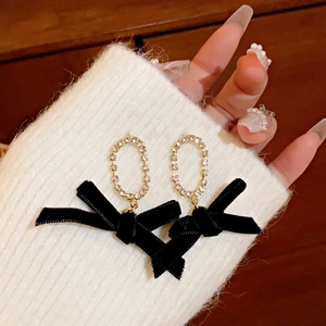Detailed view of gold pearl earrings with sparkling rhinestones and black velvet bows