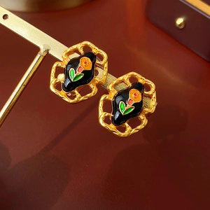 Macro shot of vintage gold earrings featuring black enamel with orange flower patterns