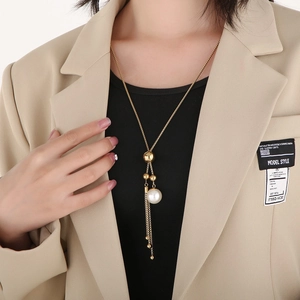 Dettaglio di una collana lunga dorata con perla e nappe metalliche eleganti