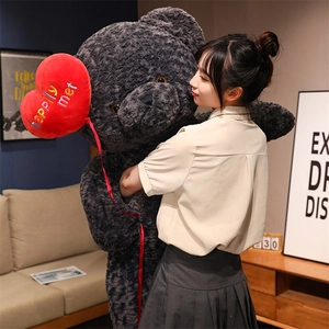 Close-up of extra large dark grey plush teddy bear with heart balloon held by model