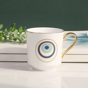 Detail shot of white ceramic evil eye mug with a luxury gold handle on a green wall background