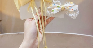 Close-up of yellow ribbon bow and white polka dot lace hair clip on a card