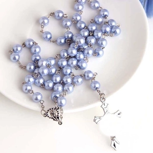 Chapelet en perles bleu clair avec croix argentée sur une assiette en céramique blanche