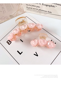 Detailed view of pink and amber heart-shaped hair claws on minimalist paper bag background
