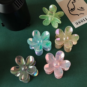 Five assorted iridescent flower hair claws in multiple colors on a dark green background