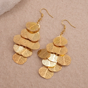 Close-up of layered golden metal disk earrings with hollow texture on beige fabric