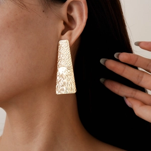 Close-up of golden geometric rectangular earrings with textured finish worn by a model