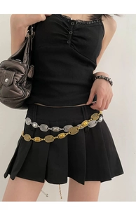 Detail of layered retro silver and gold metal waist chains on a black pleated skirt
