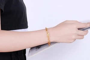 Detail of golden infinity symbol bracelet worn by a model holding a book