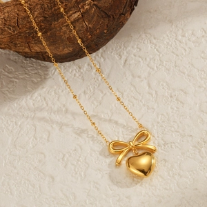 French style gold bow and heart pendant necklace displayed on a textured stone and wood