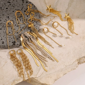 Flat lay of gold tassel, butterfly, and starfish earrings with pearls on stone background
