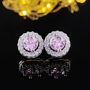 Macro detail of pink zircon halo stud earrings with silver setting on reflective surface