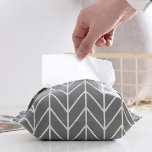 Detail of grey herringbone fabric tissue box cover with a hand pulling out a white tissue