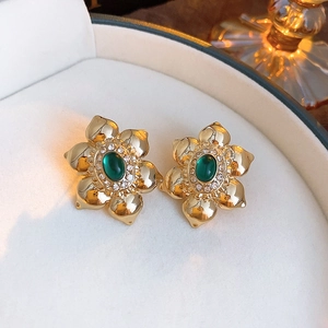 Detail view of golden flower earrings with green gemstones in a white gift box