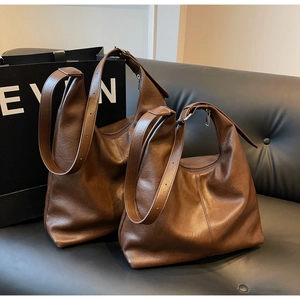 Close-up of caramel brown soft leather tote bag with wide strap on a leather sofa