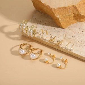 Detailed view of six pairs of gold-plated pearl earrings on minimalist stone props