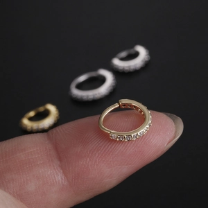 Micro copper nose ring with cubic zirconia inlay in gold and silver finishes on fingertip
