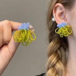 Detailed view of handmade beaded tassel earrings with blue flower and green fringe