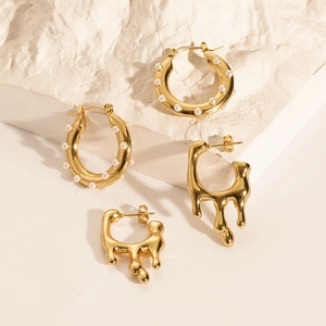 Detail of 18K gold-plated hoop earrings with pearls and liquid metal style on white rock