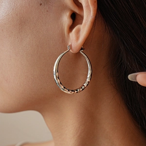 Close-up of a silver geometric hoop earring with diamond-cut texture worn by a model