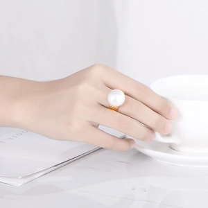 Close-up of a model wearing a large white pearl ring on gold band with a white coffee cup