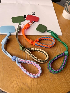 Detail of adjustable woven phone wrist straps in various two-tone colors on a wooden surface